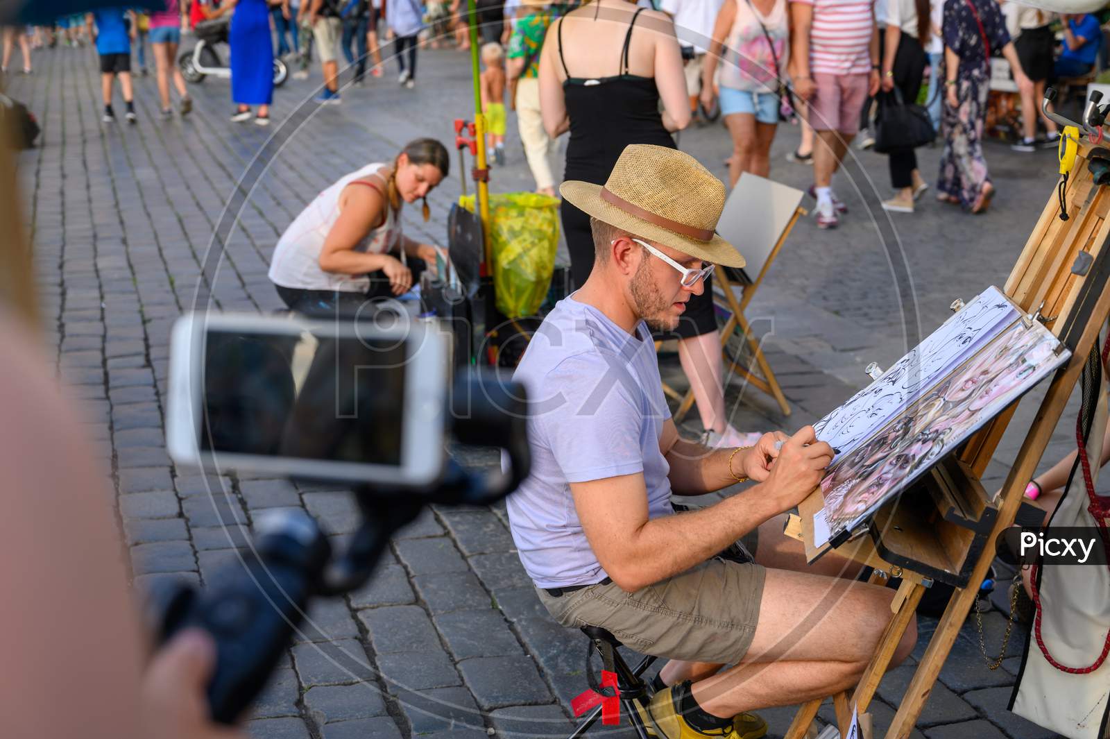 Street Caricature Artist Drawing Tourists While Being Filmed By A Smartphone On A Gimbal