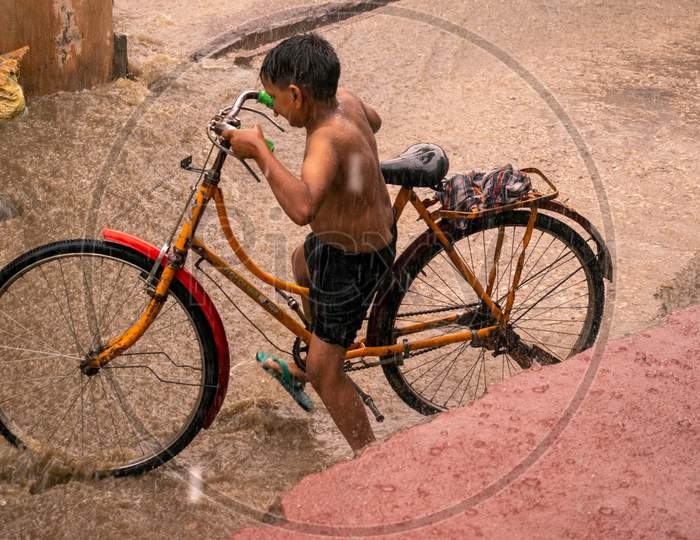 A boy rides bicycle in waterlogged streets and takes bath when it rains during monsoon in Bharatpur