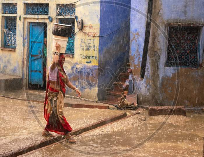 A woman carries pots on head on a road while it rains heavily during monsoon season in Bharatpur