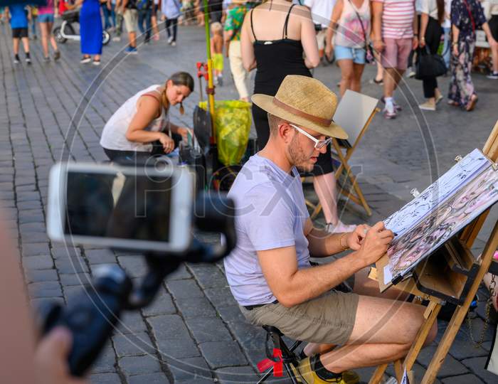 Street Caricature Artist Drawing Tourists While Being Filmed By A Smartphone On A Gimbal
