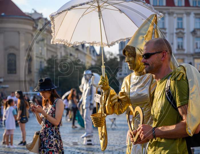 Golden Female Statue Street Performer Poses With A Male Tourist In The Old Town Square, Prague, Czech Republic