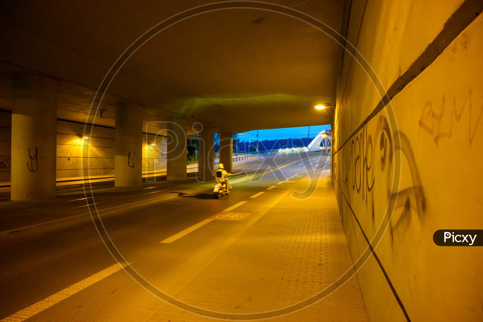 A Motioned Blurred Motor Scooter Travels Along A City Underpass At Night