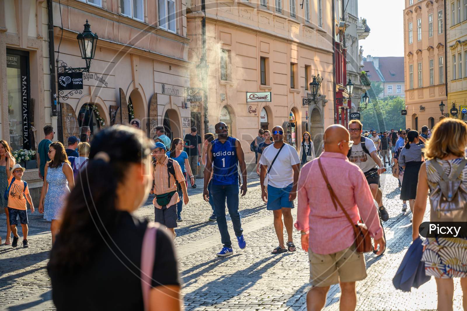 Tourists Exploring The Ancient Cobbled Streets In Old Town District Of Prague, Czech Republic In The Golden Light Of Early Evening