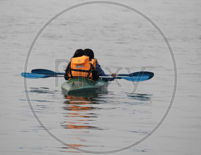 Water background with Two random people with life jacket rowing boat on a evening.