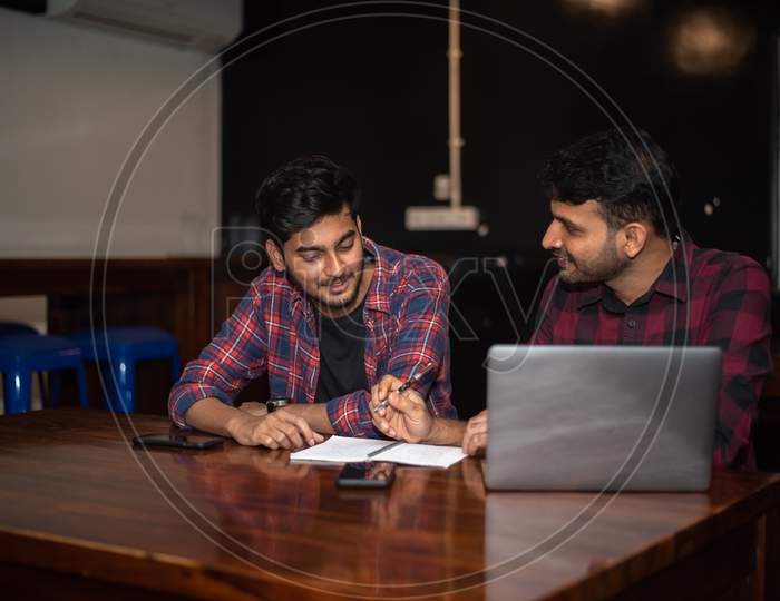 two young Indian men discussing as they work on a laptop in office
