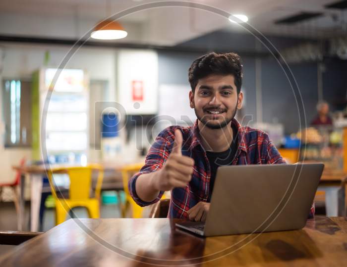 A Young Indian Man showing 'thumbs up' gesture while working on a laptop.