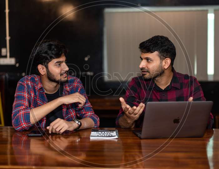 two young Indian men discussing as they work on a laptop in office