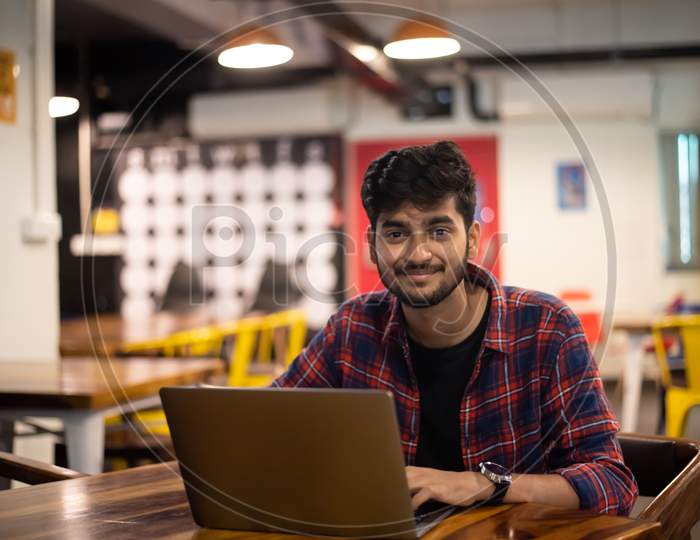 Smiling young Indian man working on a laptop in office