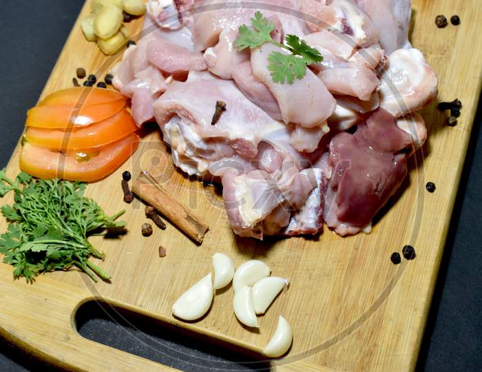 Raw chicken meat on cutting board with Onion, garlic, Coriander, Ginger and spices.