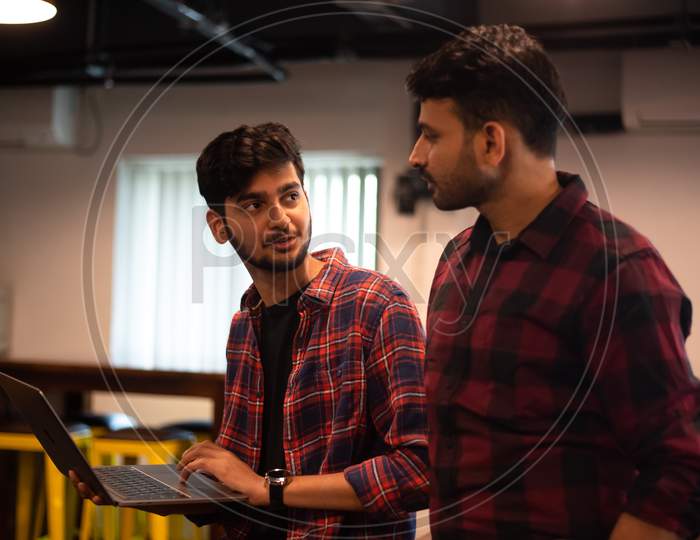 two young Indian professional men discussing as they work on a laptop in office