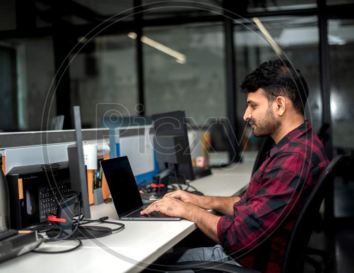 Young Indian man working on a laptop in office.