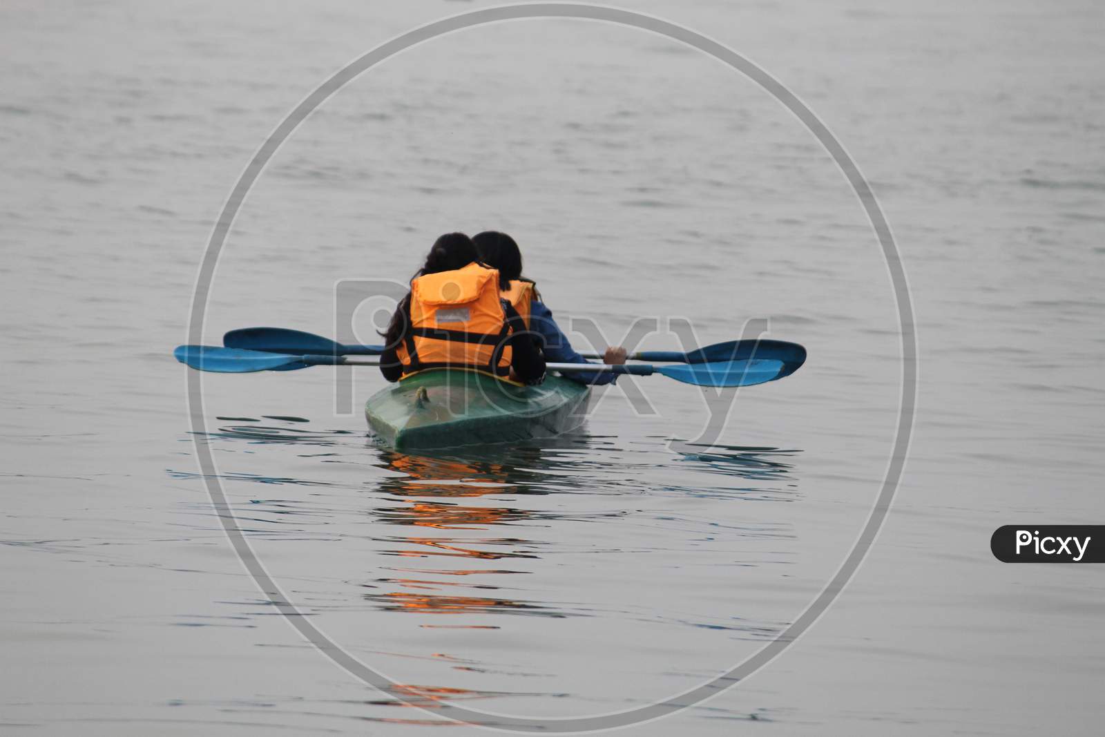 Water background with Two random people with life jacket rowing boat on a evening.