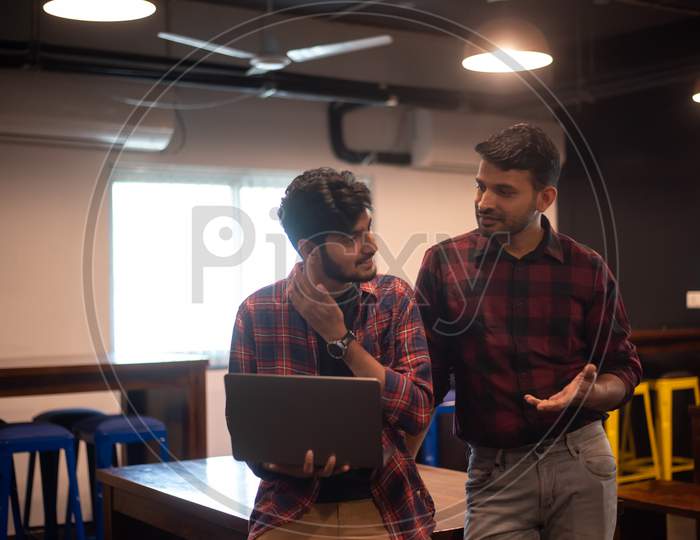 two young Indian professional men discussing as they work on a laptop in office