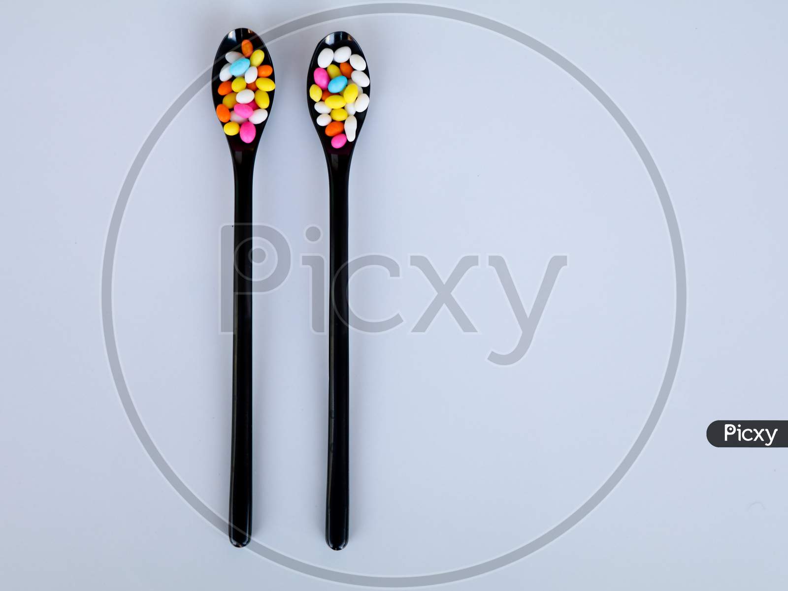 Multi Colored Fennel Sugar Candy In Black Spoons Against White Background With Copy Space, Isolated