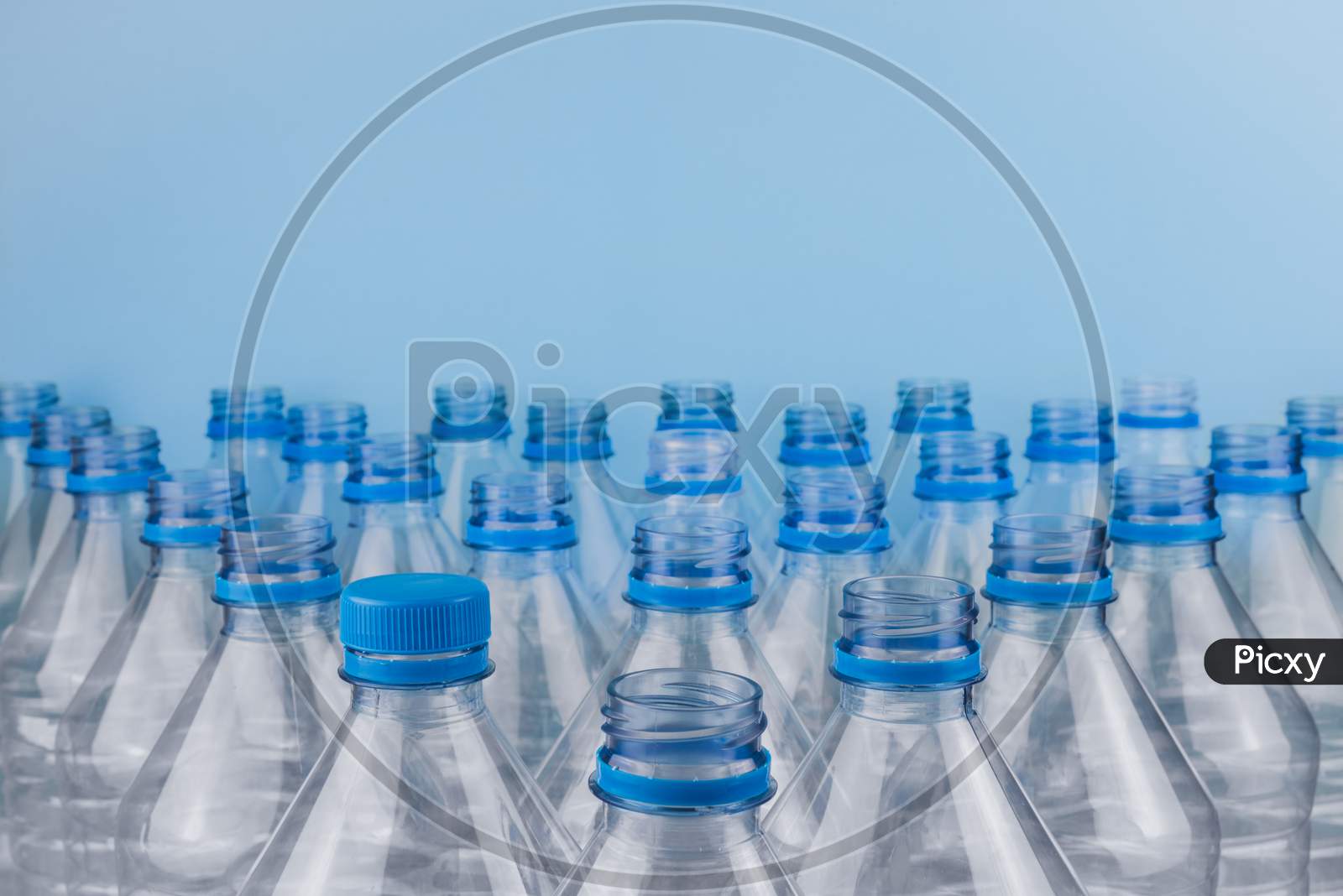 Empty Clear Plastic Bottles With Caps Stacked On A Blue Background. Recycling And Environment Concept