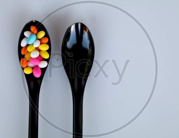 Multi Colored Fennel Sugar Candy In Black Spoons Against White Background With Copy Space, Isolated