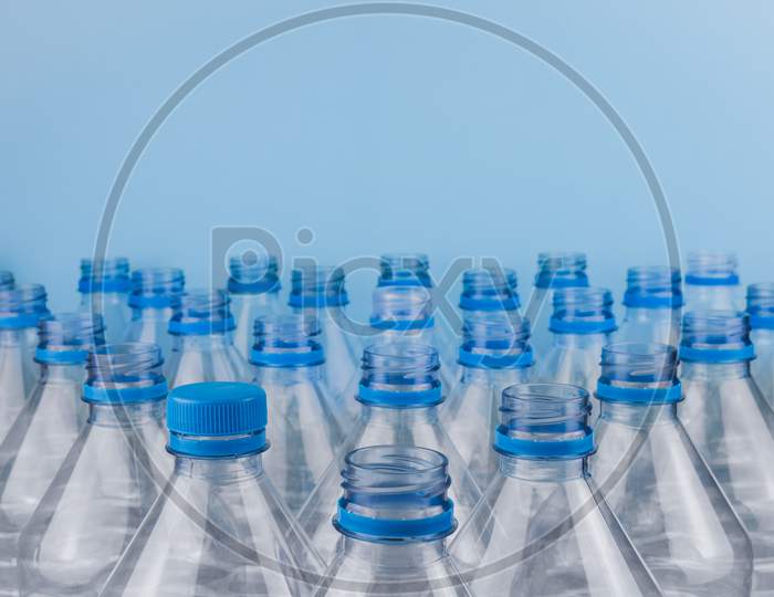 Empty Clear Plastic Bottles With Caps Stacked On A Blue Background. Recycling And Environment Concept