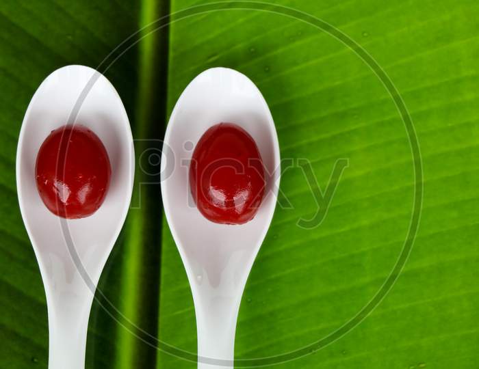 Red Color Cherry Fruits In A White Spoon Against Green Background, With Copy Space, Caption