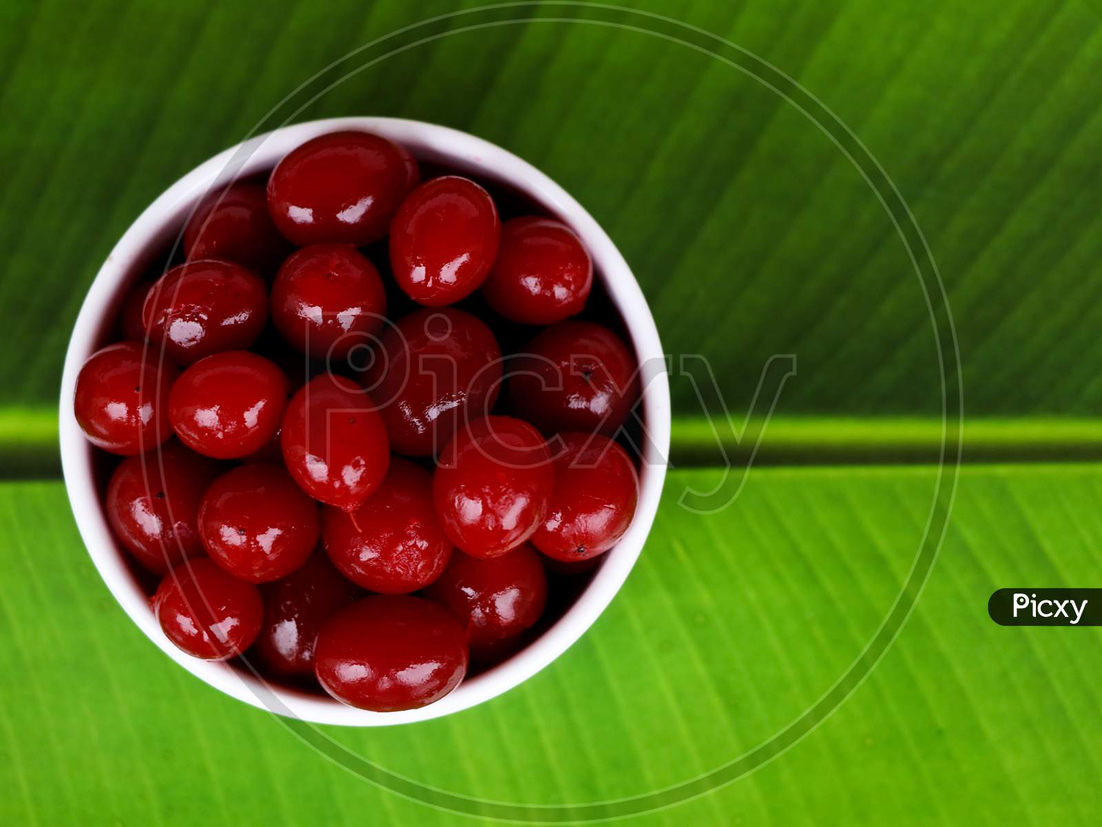 Red Color Cherry Fruits In A White Bowl Against Green Background, With Copy Space, Caption