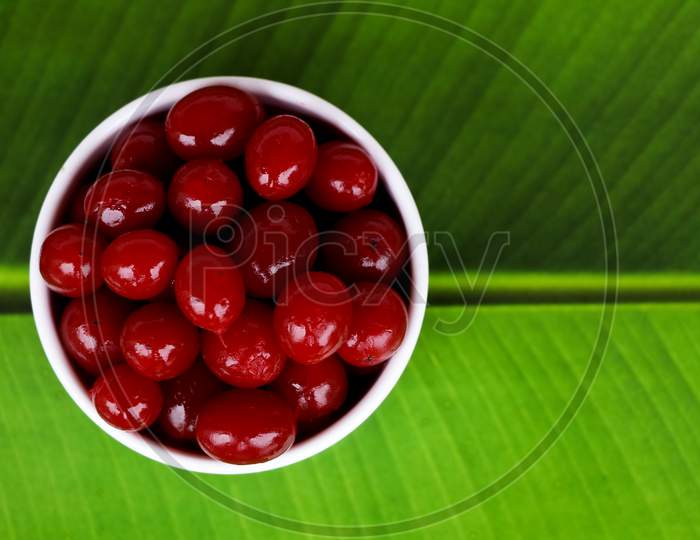 Red Color Cherry Fruits In A White Bowl Against Green Background, With Copy Space, Caption