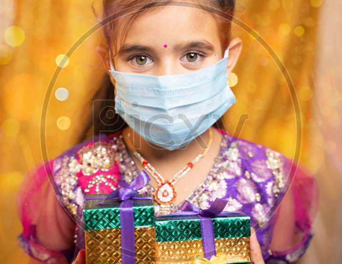 Portrait Of Girl Kid With Medical Mask Holding Gifts In Hand During Festival Ceremony - Concept Of Protection From Covid-19 Or Coronavirus During Celebrations.