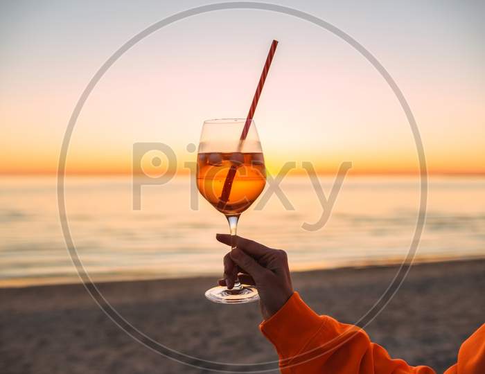 Girl Holding Glass Of Drink On Beach At Beautyfull Romantic Sunset. Glass And Hand Close Up