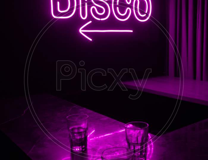 Three Alcohol Glasses Kept Under A Bright Glowing Purple Neon Disco Light Word Sign Inside A Night Club.
