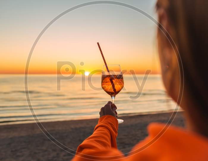 Girl Holding Glass Of Drink On Beach At Beautyfull Romantic Sunset. Glass And Hand Close Up. View From Back