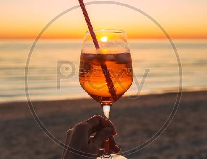 Girl Holding Glass Of Drink On Beach At Beautyfull Romantic Sunset. Glass And Hand Close Up