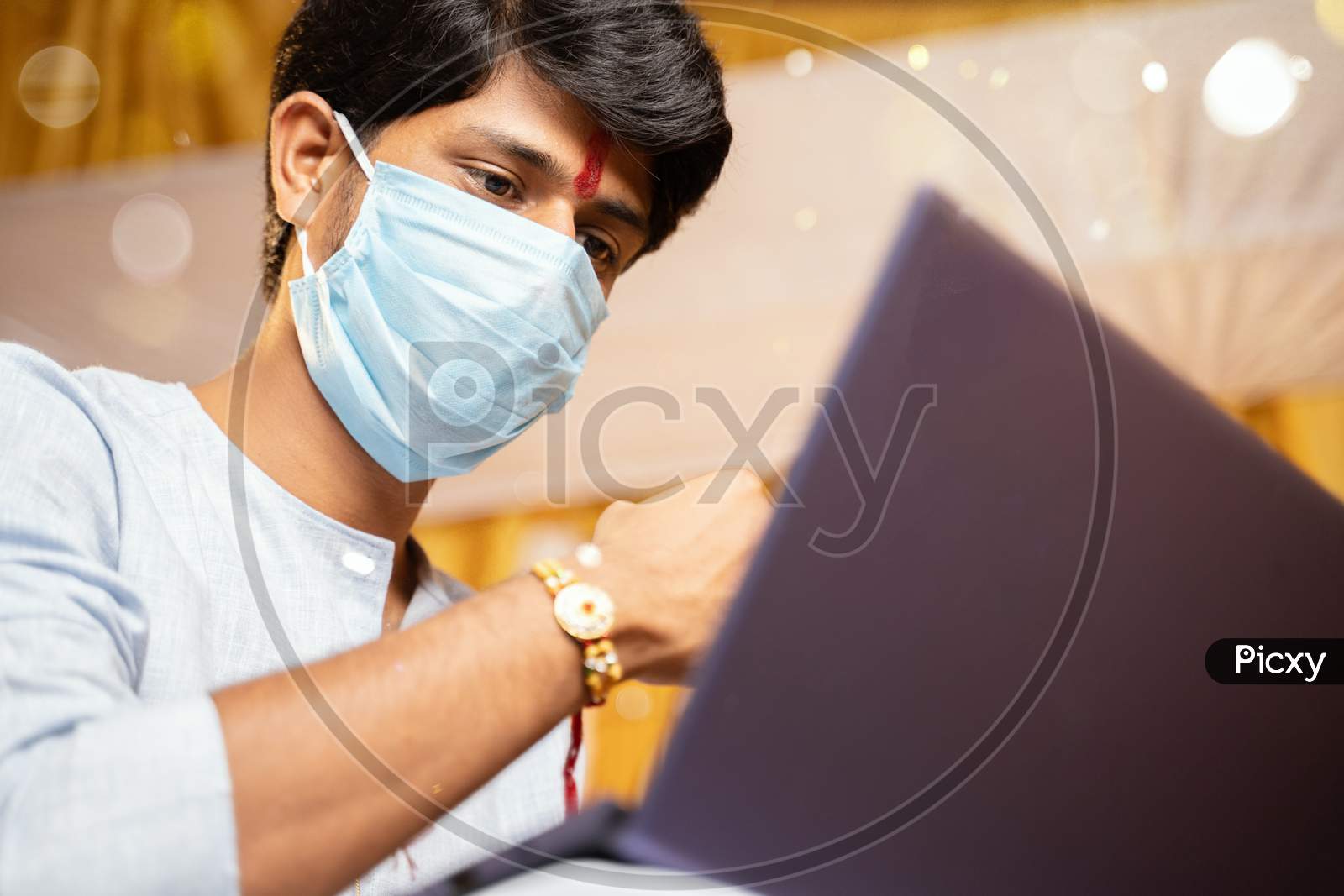 Young Man With Medical Mask Making Video Call And Showing Rakhi Or Raksha Bandhan To His Sister Or Family Friends After Festival Ceremony During Coronavirus Or Covid-19 Pandemic.
