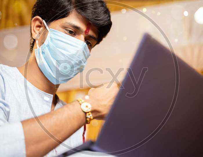 Young Man With Medical Mask Making Video Call And Showing Rakhi Or Raksha Bandhan To His Sister Or Family Friends After Festival Ceremony During Coronavirus Or Covid-19 Pandemic.