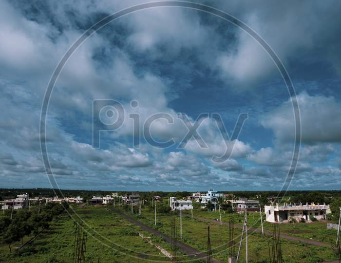 Long View Of City Landscape With Blue Sky, Clouds & Green Land