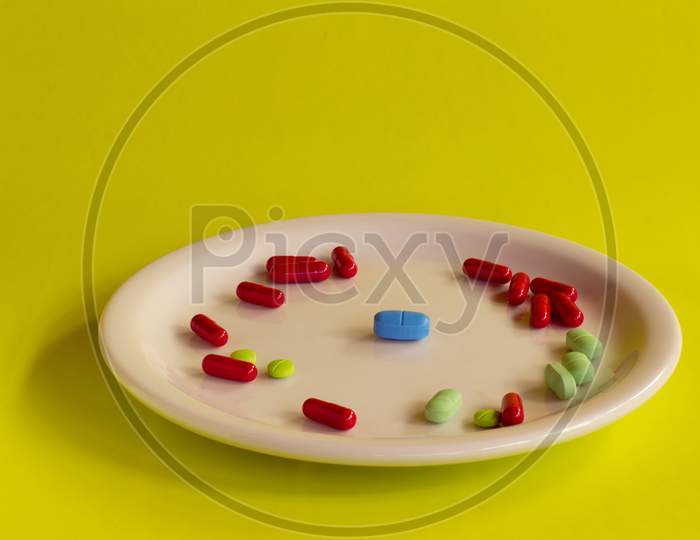 White Plate With Colored Medications On A Yellow Background.