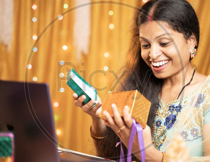 Happy Excited Woman Opening Gift In front Of Laptop During Video Call Or Chat At Raksha Bandhan Festival Ceremony - Concept Of Distance Relations, Celebrations And Lifestyle.