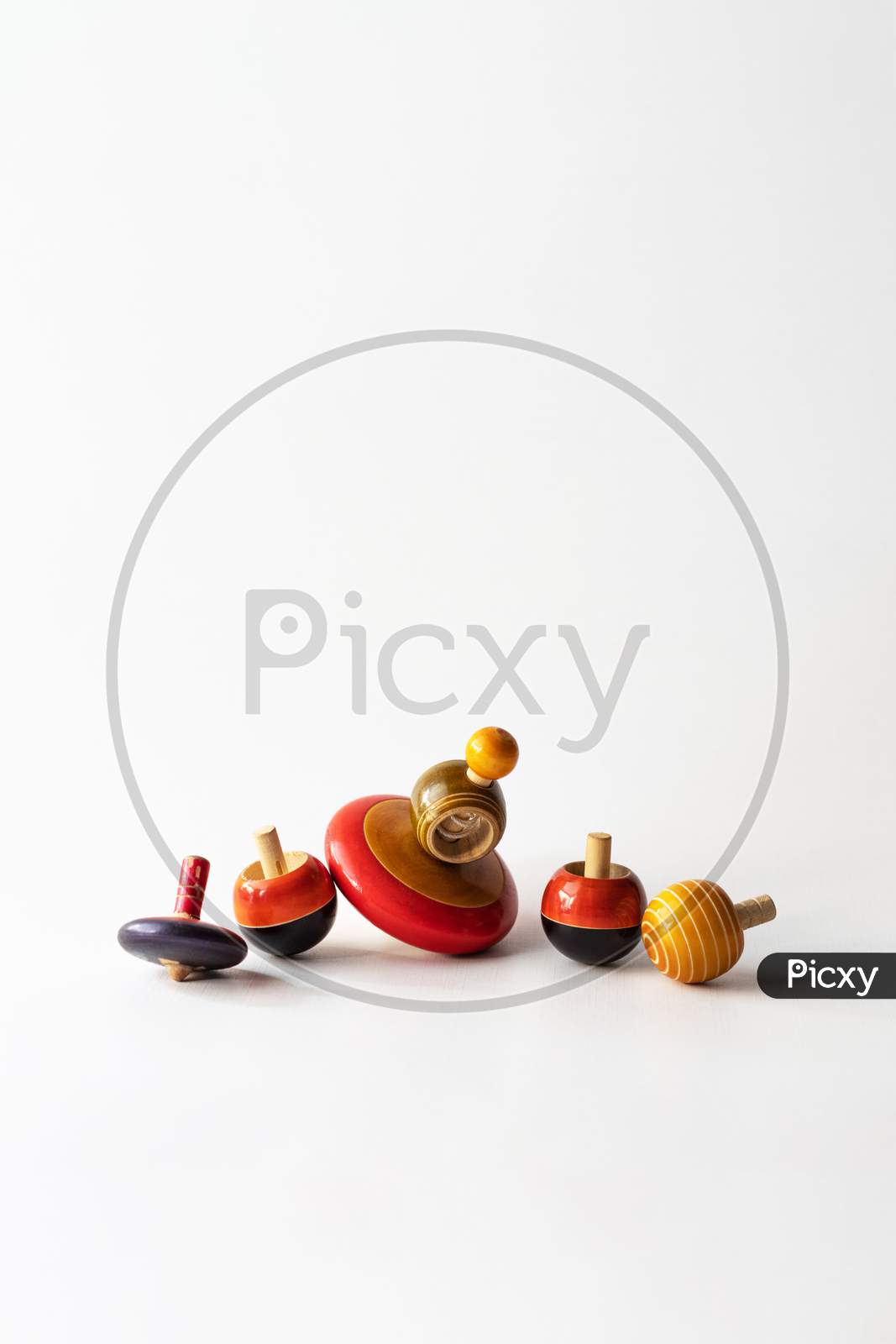 Variety of Channapatna wooden tops with bright colors against white background with copy space