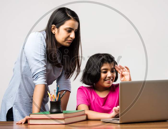 Indian / Asian Little Girl Studying Using Her Laptop Or Attending Online School At Home With Mother