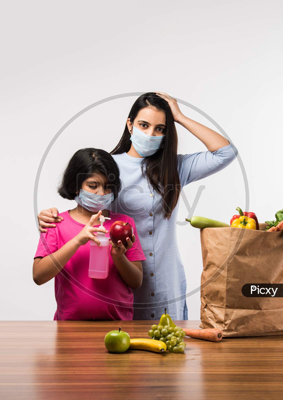 Indian mother daughter disinfecting vegetables with sanitizer while wearing face masks