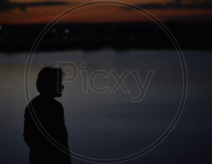 Silhouette of a young man standing by the lake
