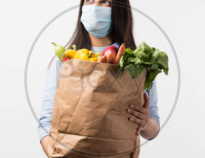 Pretty Indian Young Woman Wearing Protective Mask While Holding Paper Bag With Vegetables & Fruits