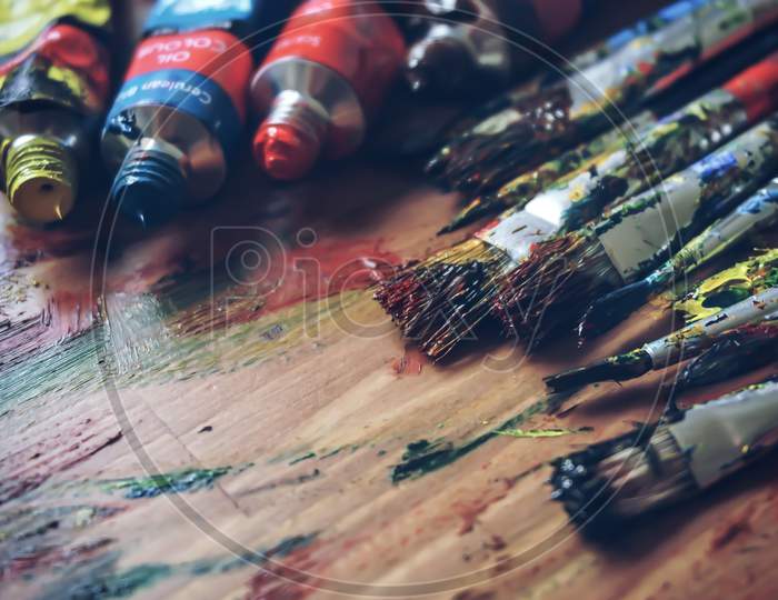 Three paint tubes near paintbrushes. ARTWORK - Messy paintbrushes