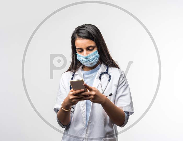 Indian Female Doctor With Stethoscope Wearing Protective Mask In Pandemic Talking On Smartphone