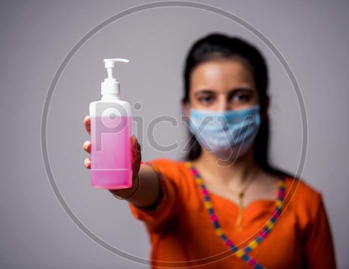 Beautiful Indian Girl Holds Sanitizer On Outstretched Arm, Focus On Bottle. Corona Virus Concept
