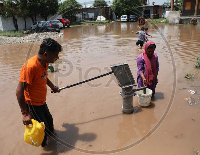 A Woman collects drinking water from a hand pump at a flooded street following monsoon rains on the outskirts in Jammu on July 29, 2020.