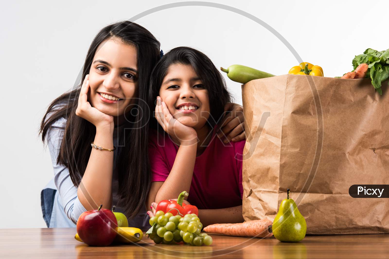 Happy Indian Family In The Kitchen. Pretty Mother & Cute Daughter Posing With Vegetables And Fruits