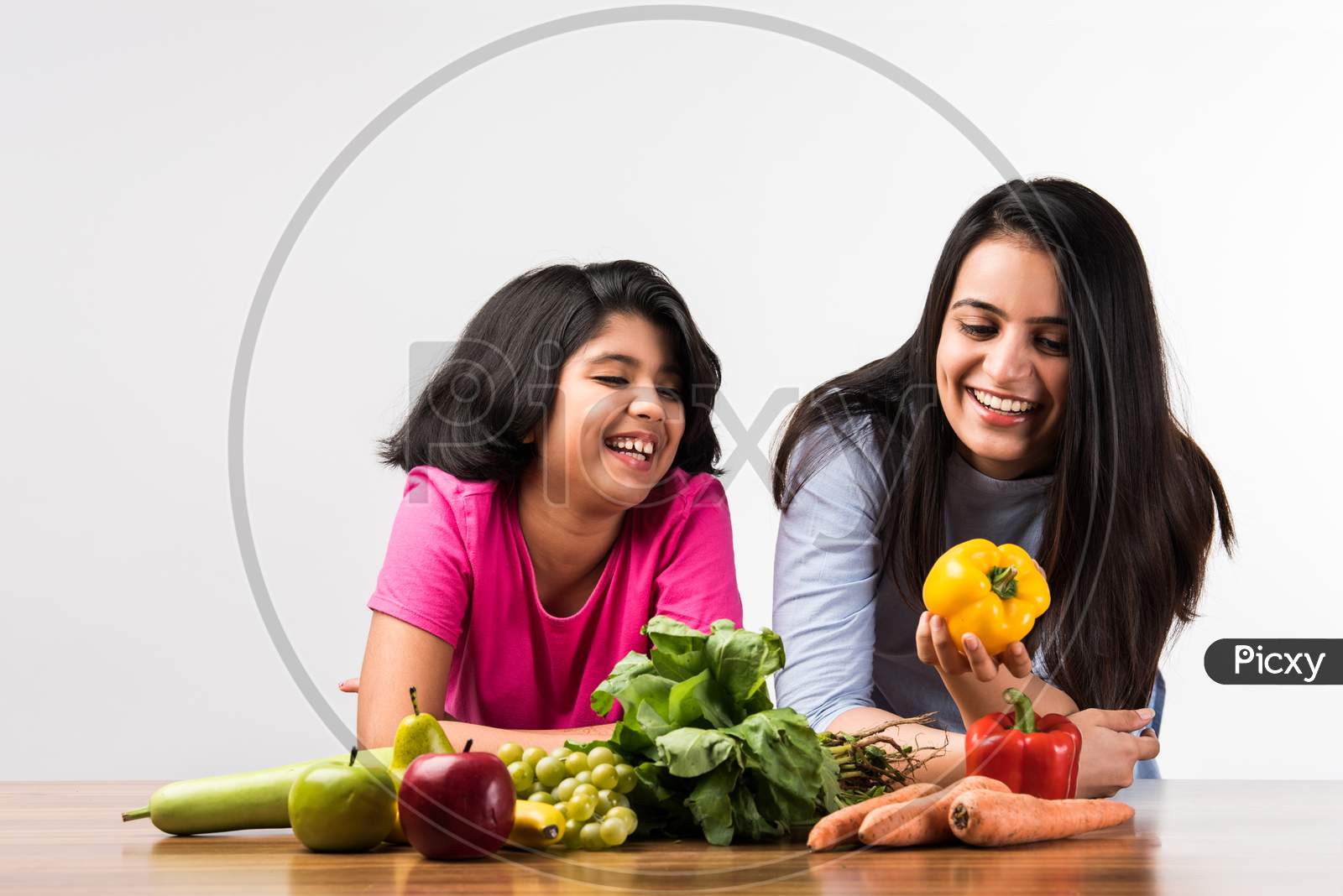 Happy Indian Family In The Kitchen. Pretty Mother & Cute Daughter Posing With Vegetables And Fruits
