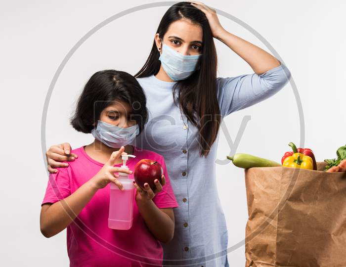 Indian mother daughter disinfecting vegetables with sanitizer while wearing face masks