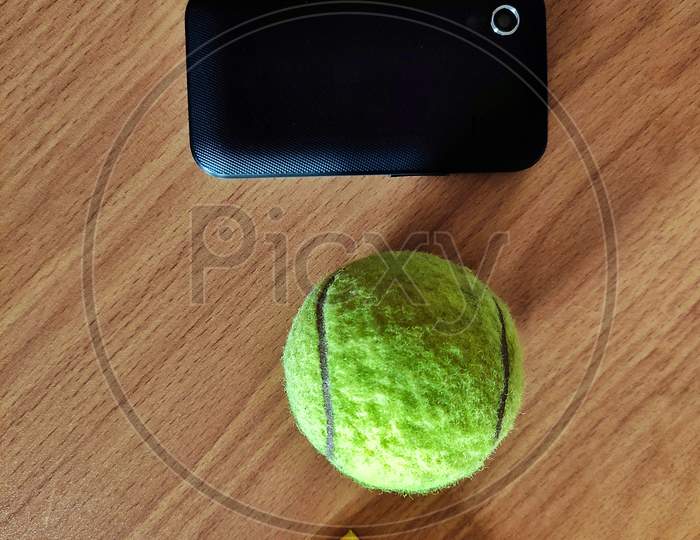A Yellow Triangular Box With A Tennis Ball And A Black Mobile.