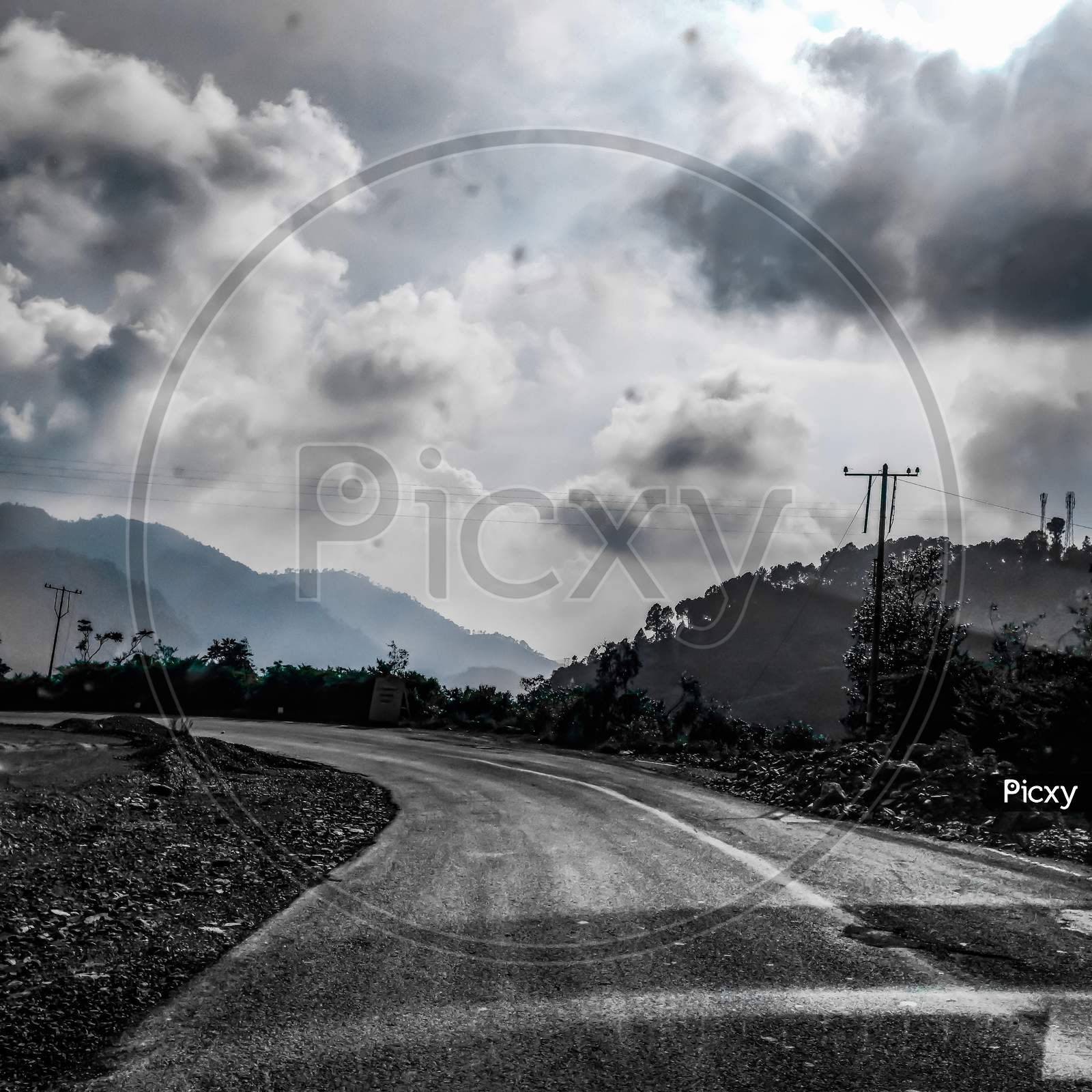 A monochrome picture of an empty road taking turn with thick clouds in the sky