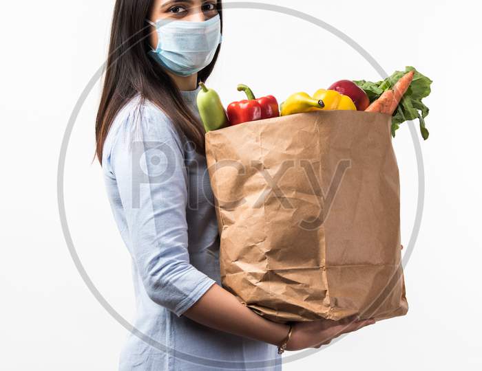 Pretty Indian Young Woman Wearing Protective Mask While Holding Paper Bag With Vegetables & Fruits