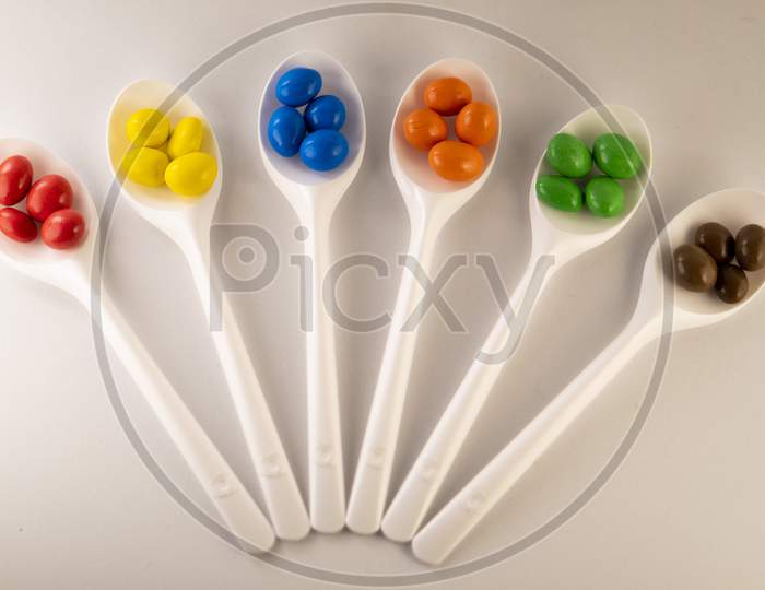 colorful chocolate balls on white  spoons on a white background.